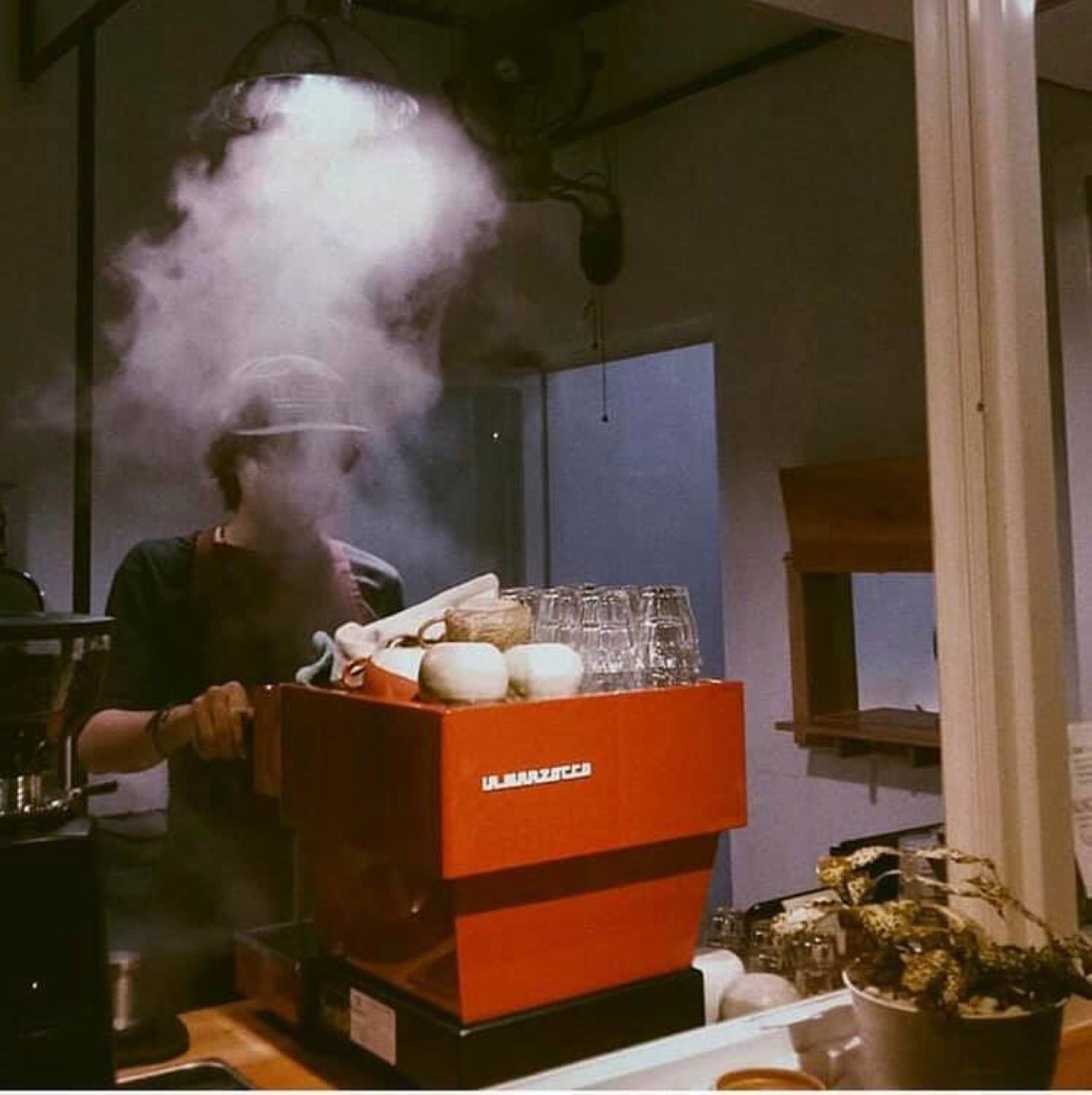 A barista brewing on an orange machine amid steam
